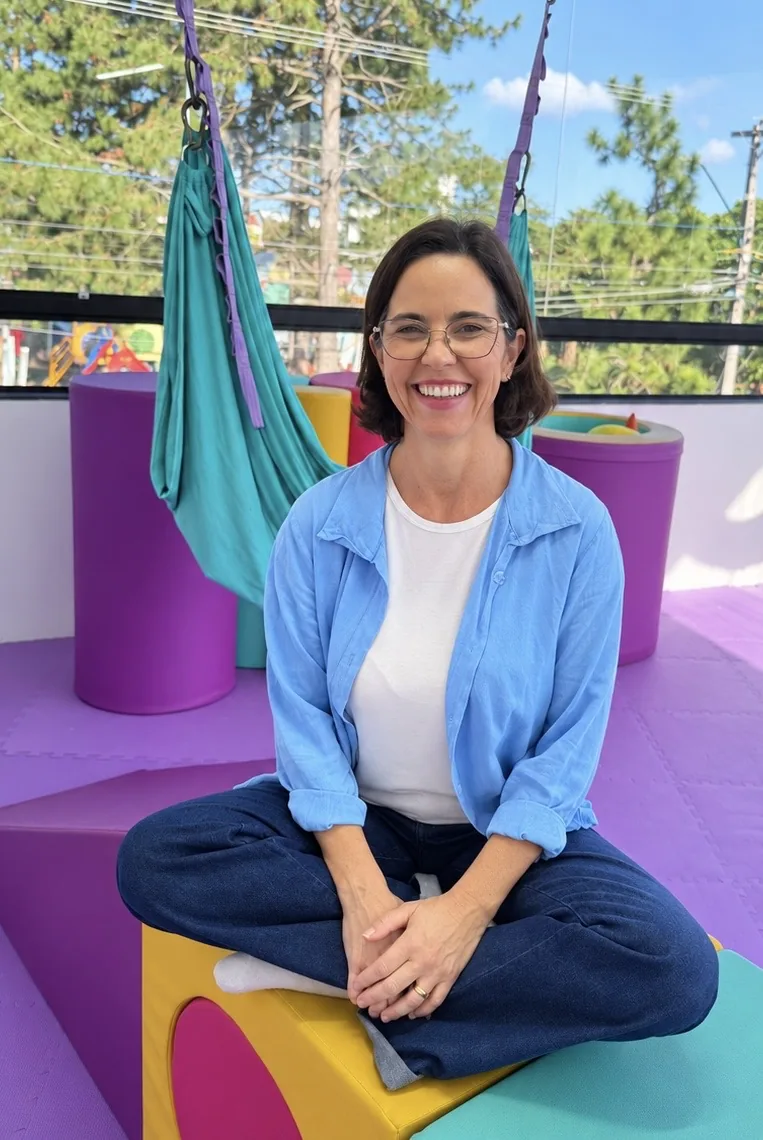 Retrato de Melissa Castro Pito Martins, sorrindo, sentada em um espaço colorido de atendimento infantil